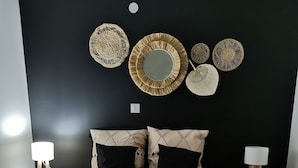 A bedroom with a black headboard, a bed with a patterned bedspread, two bedside tables with lamps, and decorative woven wall art. - Gîte des frangines (Beaumont)