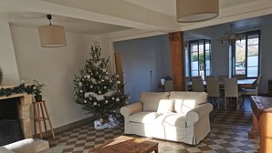 A living room with a checkered floor, a Christmas tree, a fireplace, and a dining area in the background. - Gîte des frangines (Beaumont)