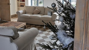 A cozy living room with a beige sofa, a coffee table, and a Christmas tree decorated with ornaments. - Gîte des frangines (Beaumont)