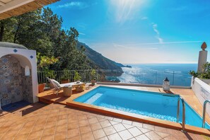 A pool area with a view of the sea, a tiled floor, and a white wall with a decorative pattern.