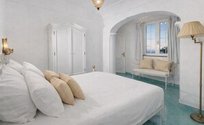A bedroom with a large bed, a white wardrobe, a bench by the window, and a floor lamp. - Villa Poesia - A Comfortable Stay (Praiano)
