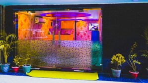 A brightly lit entrance with a yellow mat, potted plants, and a patterned wall.