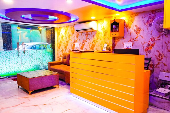 A reception area with a modern design, including a reception desk, seating area, and a wall-mounted air conditioner. - Hotel Jupiter Inn (New Delhi)