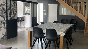 Un comedor amplio con una mesa grande y sillas negras, una escalera y un sofá gris.