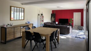 Una sala moderna con comedor, pared de acento roja, televisor de pantalla plana y estantería.