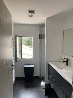 A modern bathroom with a large window, a black trash bin, and a white sink with a mirror.