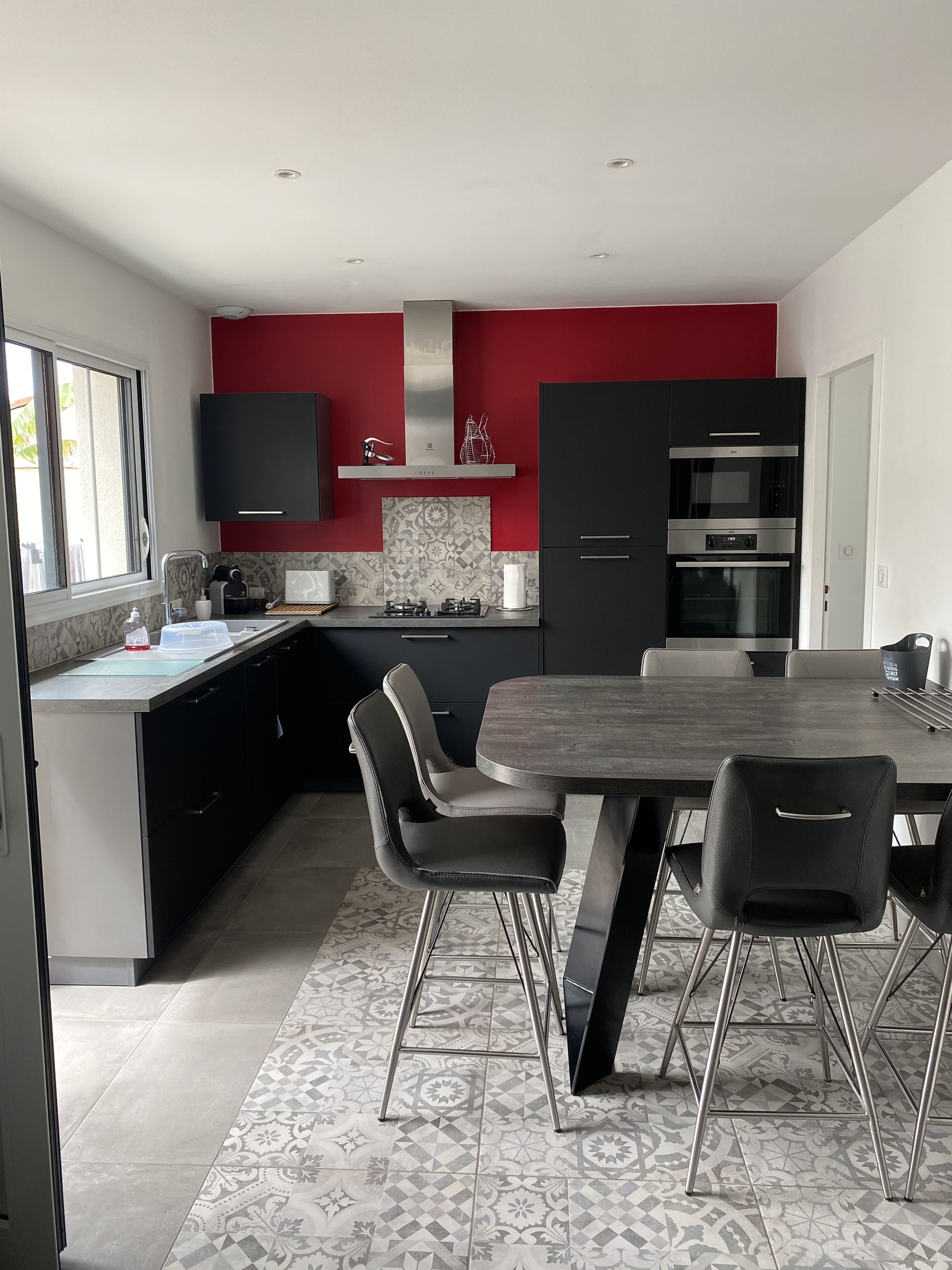 A modern kitchen with a red accent wall, stainless steel appliances, and a dining area with a dark wood table and metal chairs.