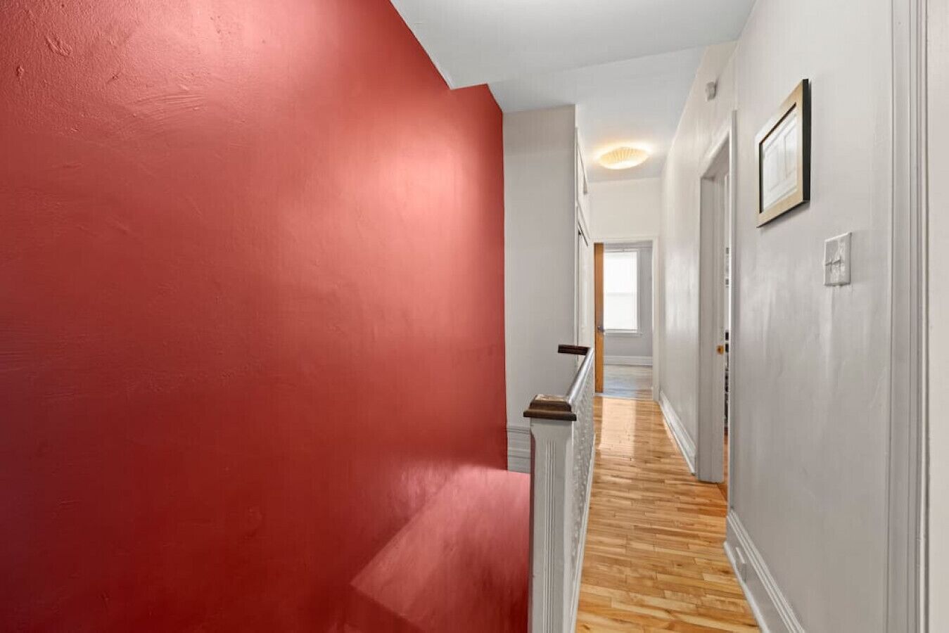 A hallway with a red wall, wooden flooring, and a white door at the end.