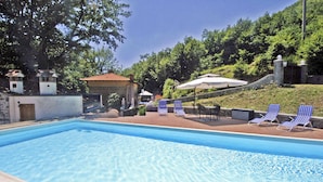 A swimming pool with lounge chairs and umbrellas, surrounded by greenery and stone structures. - Stylish Villa (6 or 8 bedrooms) with Private Pool, 40 minutes from Florence (Pistoia)