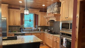 A kitchen with wooden cabinets, granite countertops, a stone accent wall, and stainless steel appliances. - Beautiful Lakefront Retreat  (Eatonton)