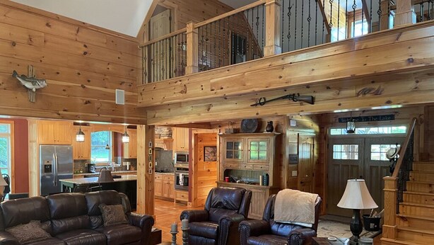 A spacious living room with leather sofas, a coffee table, and a fireplace. A kitchen is visible in the background, and there is a staircase leading to an upper level. - Beautiful Lakefront Retreat  (Eatonton)