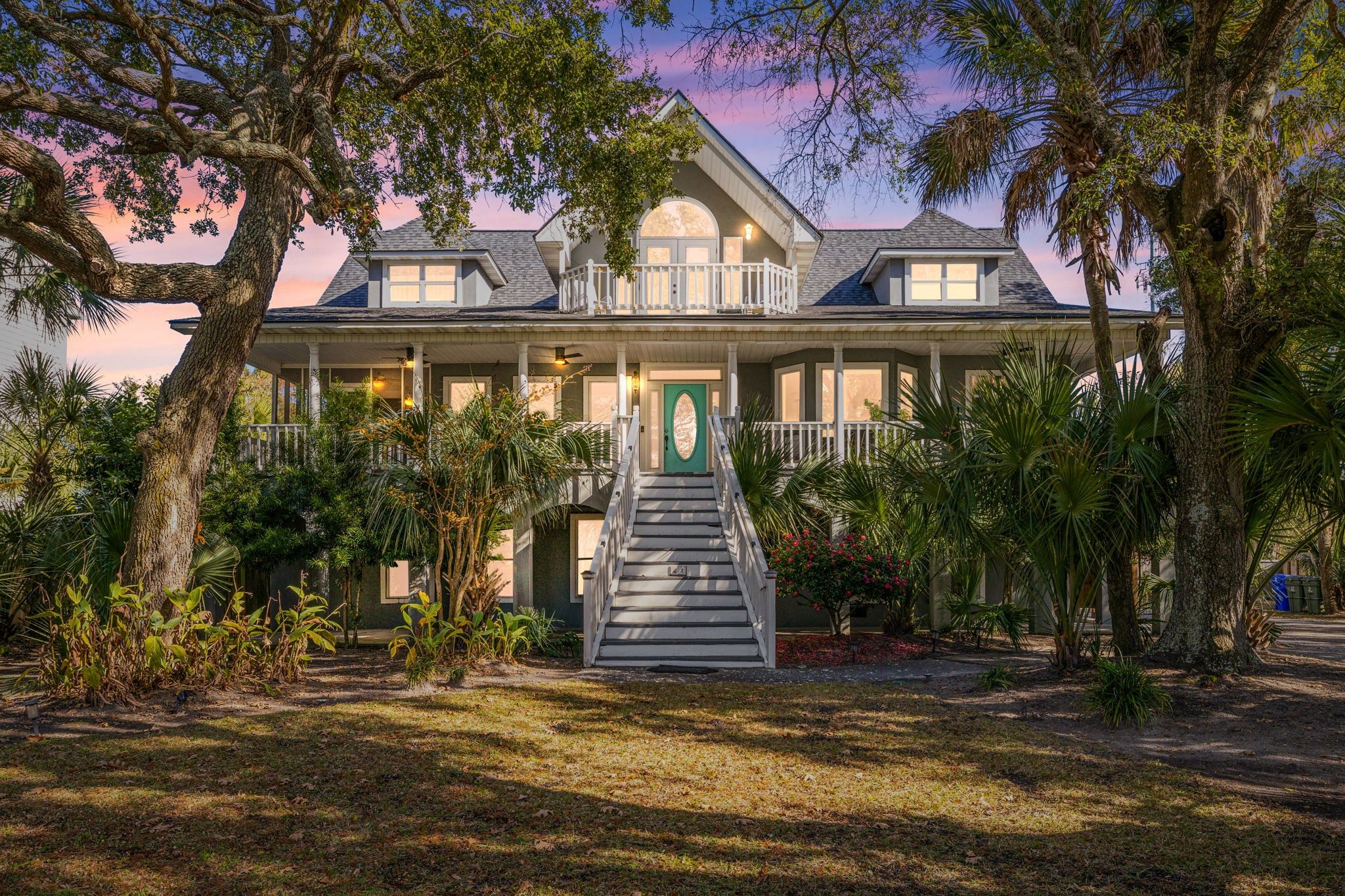 A large house with a front porch, a staircase, and a large tree in the foreground.
