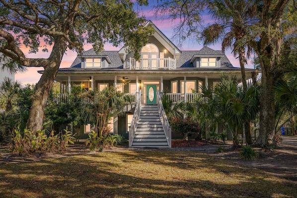A large house with a front porch, a staircase, and a large tree in the foreground.