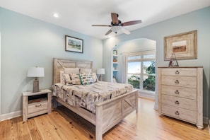 A bedroom with a wooden bed, a nightstand, a dresser, and a ceiling fan.