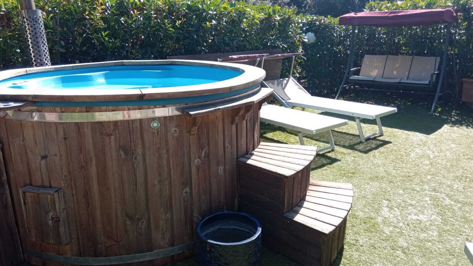 Una bañera de hidromasaje de madera con escalones y una escalera, rodeada por un jardín cubierto de césped y una valla de madera.