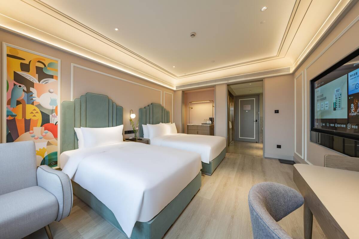 Une chambre d’hôtel avec deux lits, un bureau, une chaise, une télévision et une salle de bain visible à travers une porte ouverte.