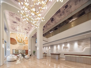 Un hall d’entrée spacieux avec un plafond haut, des sièges modernes et un comptoir d’accueil.