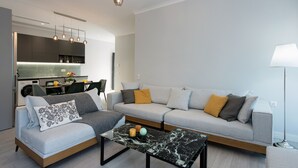 A modern living room with a sofa, coffee table, and a kitchen in the background. - PELAGIA SUITES (Corfu)