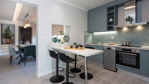 A modern kitchen with a white island, black bar stools, and stainless steel appliances. - PELAGIA SUITES (Corfu)