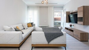 A modern living room with a sofa, TV, and wooden cabinets. - PELAGIA SUITES (Corfu)