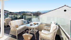 A balcony with wicker furniture, a glass table, and a view of the city. - PELAGIA SUITES (Corfu)