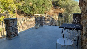 Une terrasse avec un mur en pierre, une clôture en métal, une table et une chaise.