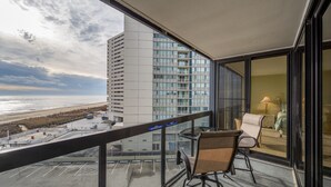 Un balcón con vista a la playa y un edificio alto. Hay una silla y una mesa en el balcón.