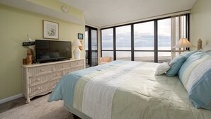 Un dormitorio con una cama grande, un televisor en una cómoda y vistas al océano a través de amplios ventanales.