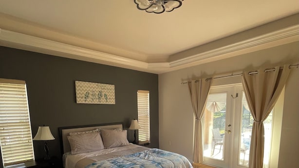 Een slaapkamer met een bed, een plafondventilator, een raam met gordijnen en een aan de muur hangend schilderij.