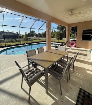 A covered outdoor area with a pool, a table with chairs, and a ceiling fan.