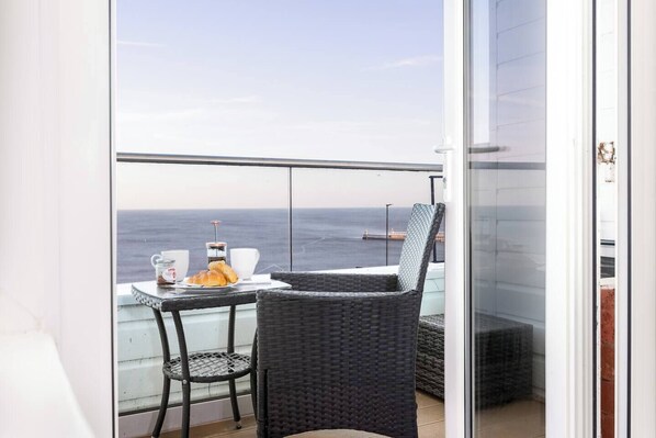 A balcony with a table set for breakfast, overlooking the sea.