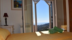 Habitación de hotel con cama, lámpara, un cuadro y vista al mar por una puerta abierta.