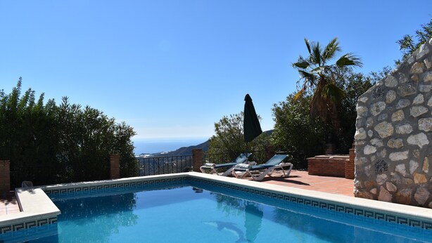 Una piscina con sillones de descanso y un muro de piedra, rodeada de vegetación y vistas al océano.
