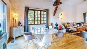 Un salón amplio con una mesa de comedor redonda, sillas blancas, techo de madera y un ventanal grande.