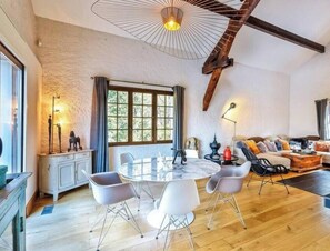 A spacious living area with a round table, modern chairs, a sofa, and a large window with curtains.