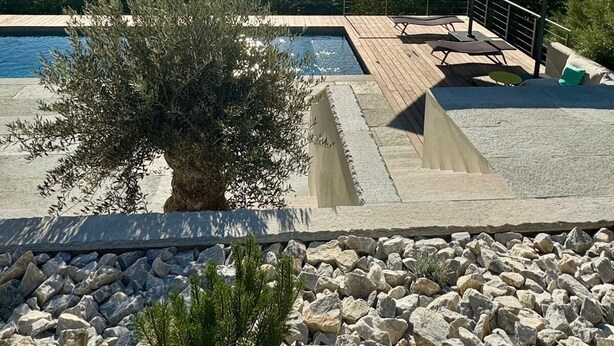 Un área de piscina con cubierta de madera, sillas de descanso y un pérgola.