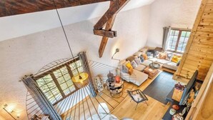 Un loft espacioso con techo alto, una escalera en espiral, una zona de estar acogedora con sofá y sillones, y una mesa de comedor.