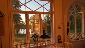 A dining area with a table set for two, large windows with a view of a lake, and a chandelier. - Seaside century house with beautiful sunset and big jetty with sauna  (ljusterö)