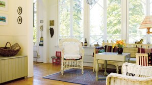 A cozy room with wicker furniture, a table with a vase of flowers, and a large window with a view of trees. - Seaside century house with beautiful sunset and big jetty with sauna  (ljusterö)