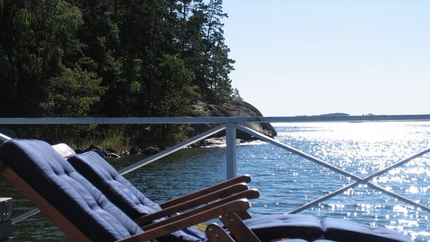 A wooden deck with two lounge chairs facing a body of water, surrounded by trees and a railing. - Seaside century house with beautiful sunset and big jetty with sauna  (ljusterö)