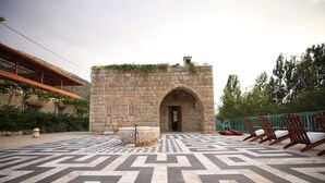 Un patio con un muro de piedra, piso a cuadros y sillas de madera.