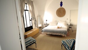 Un dormitorio con cama, mesitas de noche, un sillón de lectura y un ventanal con cortinas.