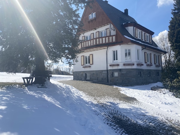 Une maison à deux étages, avec des fondations en pierre, un balcon en bois et une allée pavée.