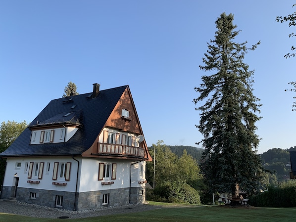 A two-story house with a steeply pitched roof, stone foundation, and multiple windows with shutters.