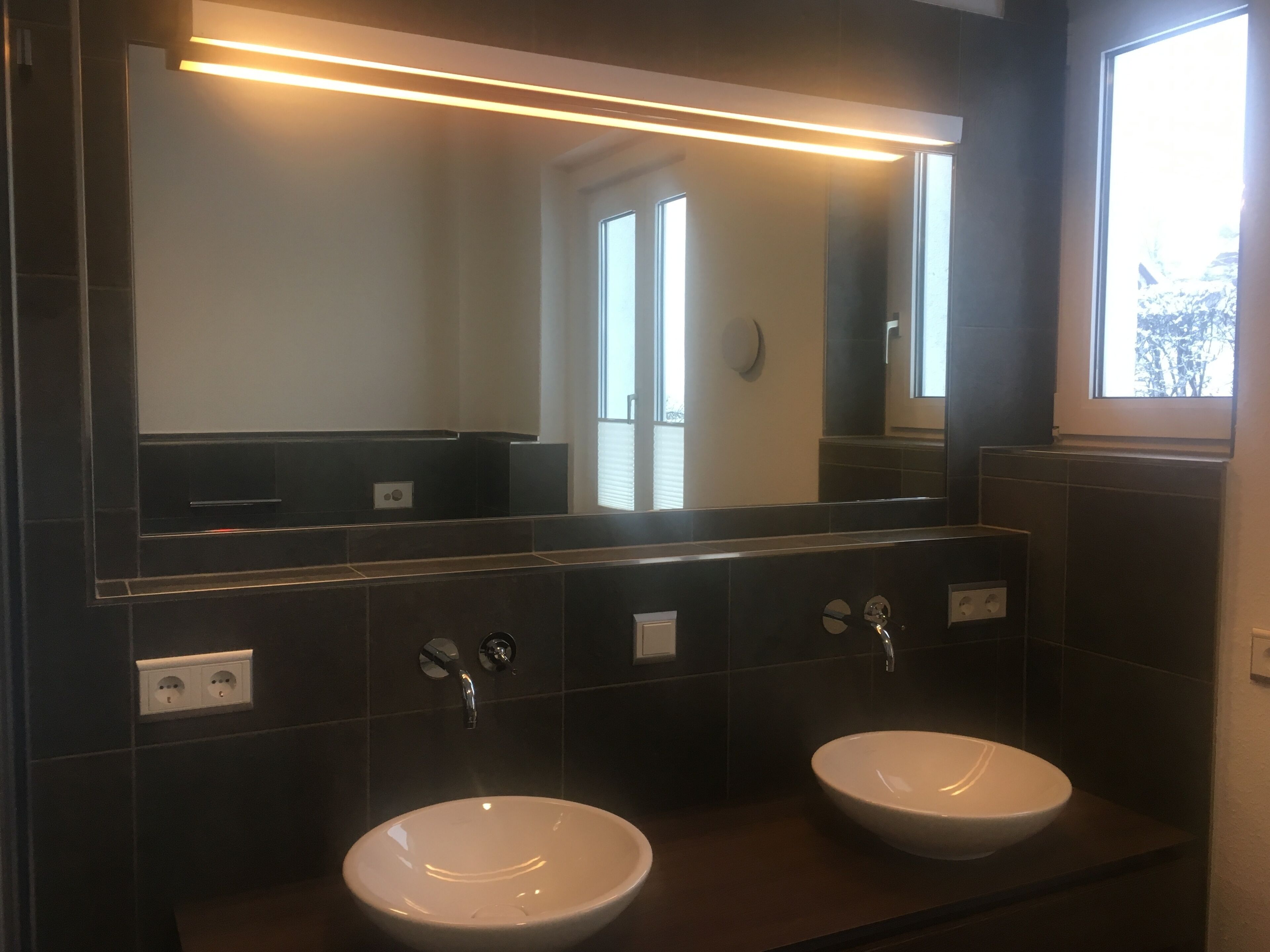 Een badkamer met twee wastafels, een grote spiegel en een raam.