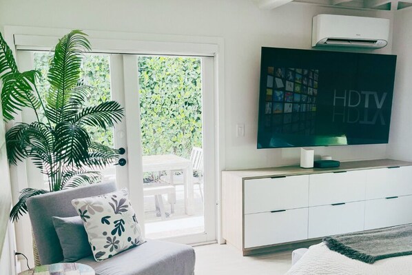 A modern living room with a flat-screen TV, a sofa, a coffee table, and a large plant.
