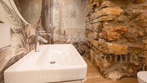 Un baño con un lavamanos blanco, una ducha con puerta de cristal y una pared de piedra.