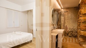 Un dormitorio con cama, un baño con lavamanos y espejo, y una pared de piedra.