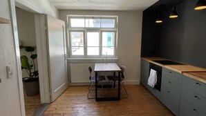 Eine Küche mit Holzboden, Tisch mit Stühlen, einem Fenster mit Jalousien und einer schwarzen Arbeitsplatte.