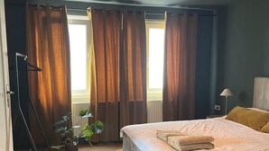 Ein Schlafzimmer mit Bett, Vorhängen, einer Stehlampe, einer Stehsteckdose und einer Zimmerpflanze.